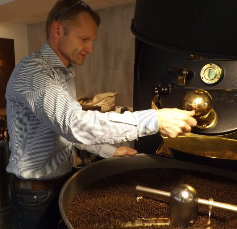 Kaffeeröster bedient eine Maschine, während frisch geröstete Bohnen auf der Oberfläche liegen.